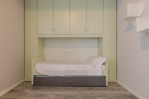 Camera moderna all'Hotel Prince Garda a Serniga con letto incorporato, biancheria bianca e armadietti contenitori