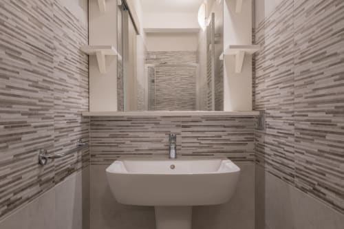 Bagno moderno dell'hotel Prince Garda a Serniga con piastrelle a righe grigie e lavabo bianco su piedistallo