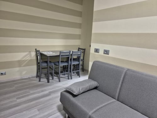 Pareti a righe grigie, moderno divano grigio, tavolo da pranzo con sedie, pavimento in legno nell'appartamento Mia Monza Living