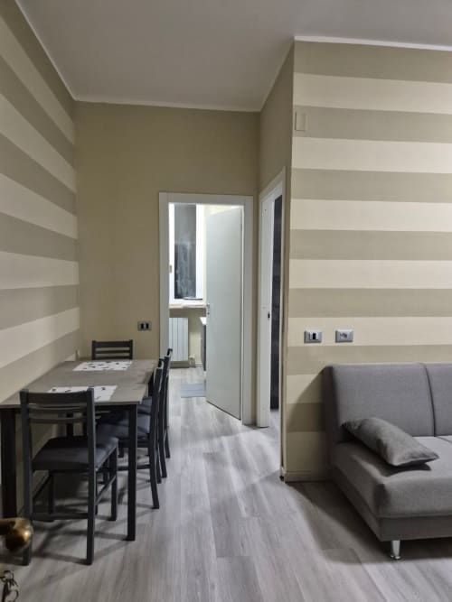 Elegante zona living dell'appartamento Mia Monza con pareti a righe, tavolo da pranzo, divano grigio e angolo cottura a Monza, Italia