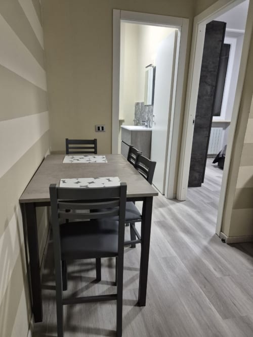 Moderna zona pranzo nell'appartamento Mia Monza Living con sedie nere, tavolo grigio e corridoio verso il bagno.