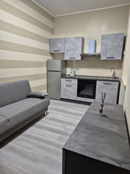 Monolocale moderno presso Mia Experience Monza con cucina, divano grigio e parete con motivi a righe