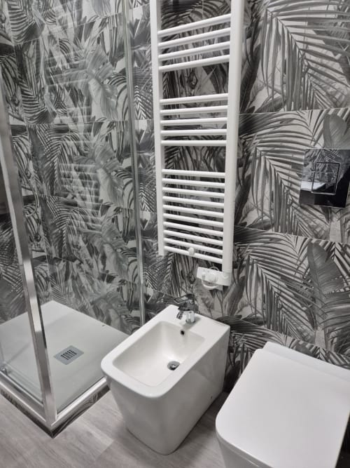 Bagno moderno con carta da parati a motivi di palme tropicali, sanitari bianchi, bidet, wc, box doccia e scaldasalviette