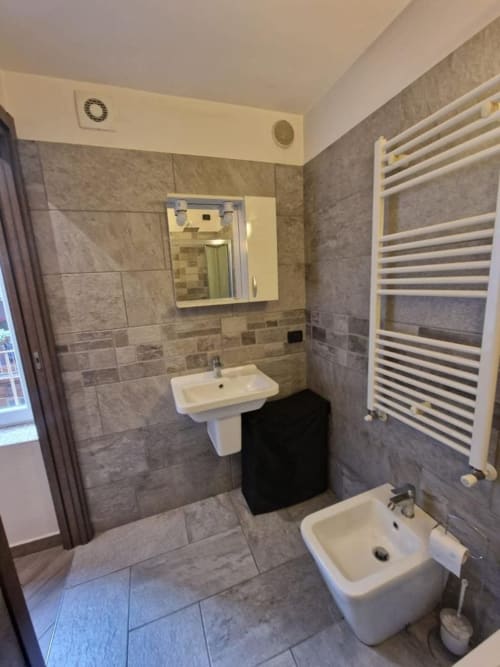 Bagno moderno nella suite Mia Monza con piastrelle grigie, lavabo bianco, WC, scaldasalviette e specchio