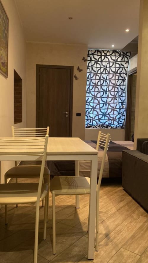 Moderna zona pranzo nella Suite Mia Monza con sedie bianche, tavolo in legno e pannello finestra geometrico