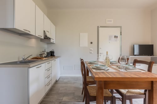 Moderna cucina e zona pranzo dell'hotel Prince Garda a Serniga con tavolo in legno, mobili bianchi e TV
