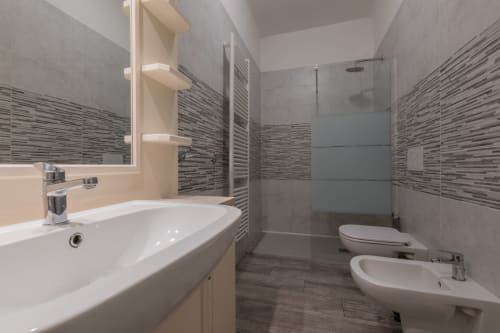 Moderno bagno dell'hotel Prince Garda a Serniga con doppio lavabo, doccia in vetro e dettagli in piastrelle a righe