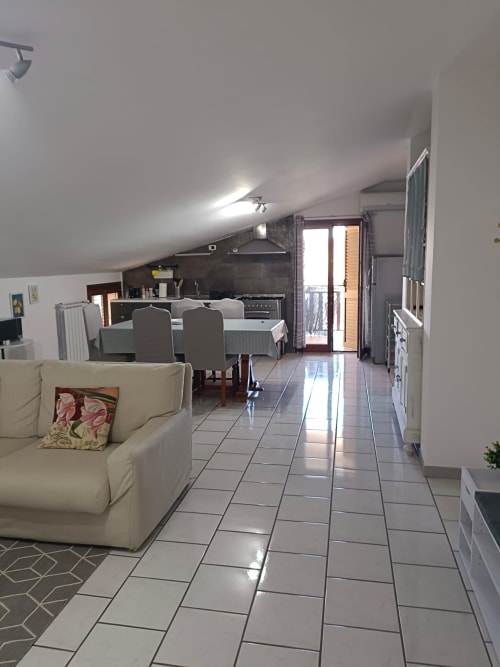 Open-plan living area in Atessa apartment with cream sofa, dining table, kitchen, and glass doors opening to balcony with