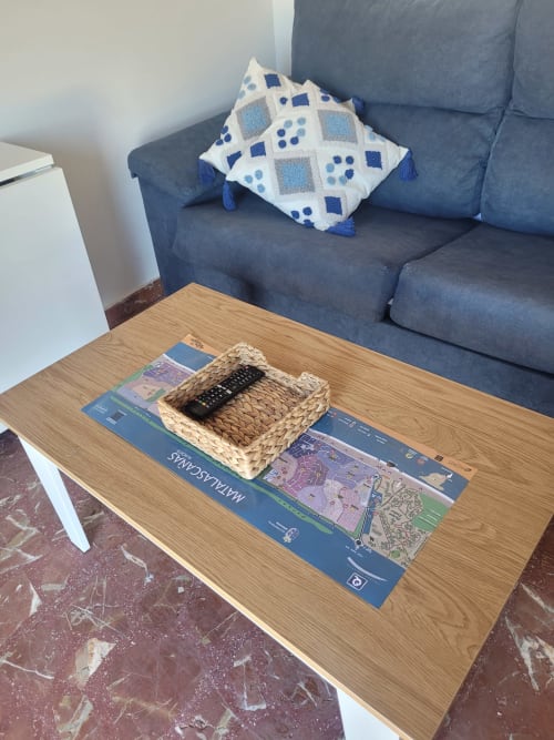 Sala de estar con sofá azul, cojín decorativo, mesa de centro de madera con cesta tejida y control remoto en Apartamentos A la