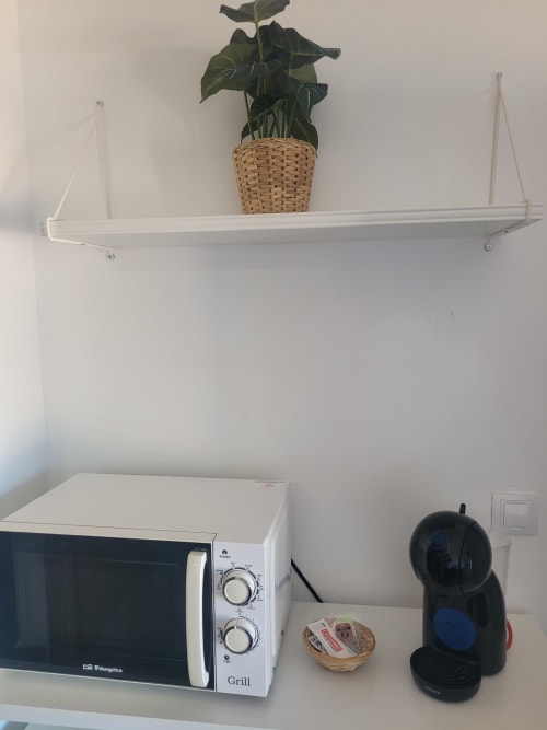 Rincón de cocina con microondas grill, cafetera y planta en maceta sobre repisa blanca en apartamento frente al mar