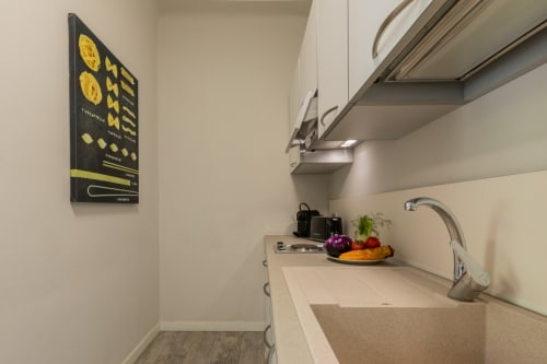 Piccola cucina moderna dell'hotel Prince Garda a Serniga con elettrodomestici compatti, ciotola di frutta sul bancone e lavagna menu gialla