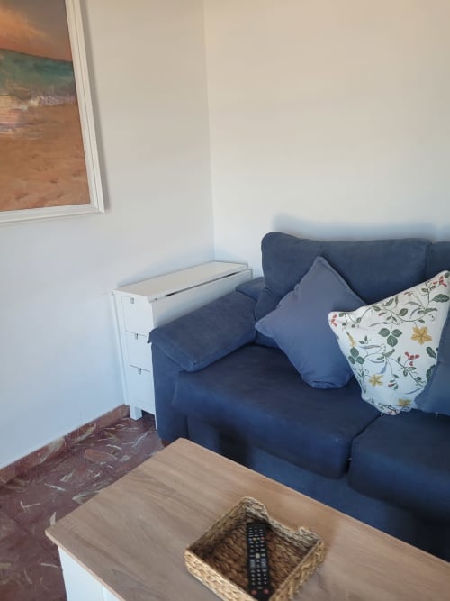 Acogedor salón en apartamento frente al mar con sofá azul marino, arte costero y vistas al océano en Matalascañas