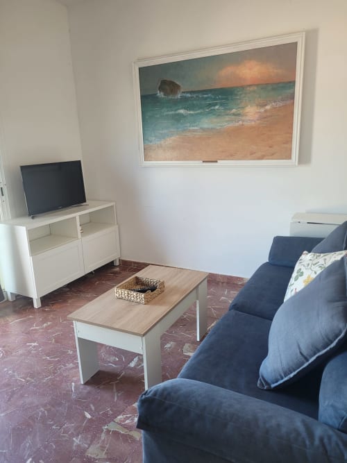 Sala de estar con vista al mar, sofá azul, televisor y mesa de café de madera en apartamento frente al mar en Matalascañas