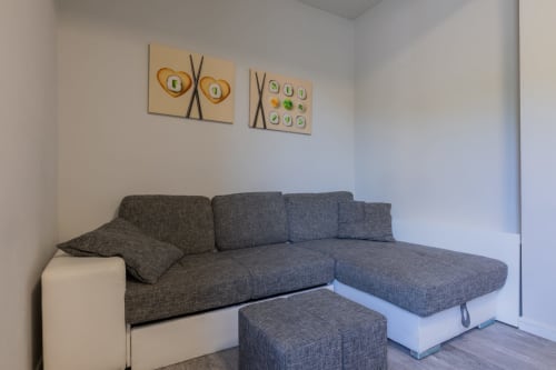 Divano componibile grigio moderno con cuscini e pouf nella suite dell'hotel Prince Garda a Serniga