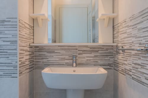 Bagno moderno dell'hotel Prince Garda a Serniga con lavabo a colonna bianco, rivestimento in piastrelle righe e specchio.