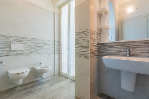 Bagno moderno dell'hotel Prince Garda a Serniga con sanitari bianchi, parete rivestita di piastrelle a righe, lavabo a colonna e vetro
