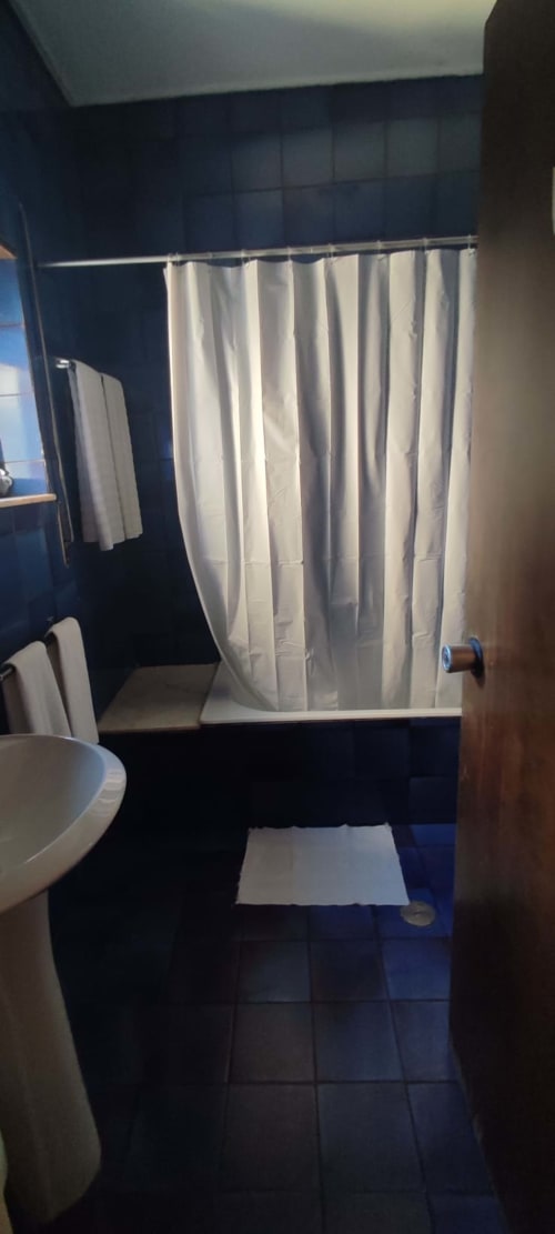 Modern bathroom at Porta 80 House Braga with dark tiles, white shower curtain, toilet, and towel rail