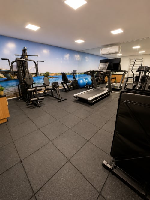 Centro de fitness moderno com equipamentos de exercício, esteira, bola de estabilidade azul e mural do espaço aquático em hotel de Brasília