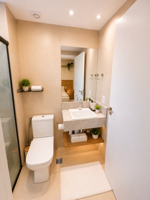 Banheiro moderno em apartamento de Brasília com vaso sanitário branco, pia de pedra, espelho e iluminação acolhedora