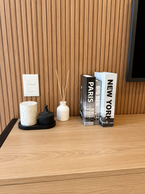 Decoração de apartamento moderno com difusor cerâmico branco, livros sobre Paris e Nova York, e móveis em madeira clara na ALUGUEASY