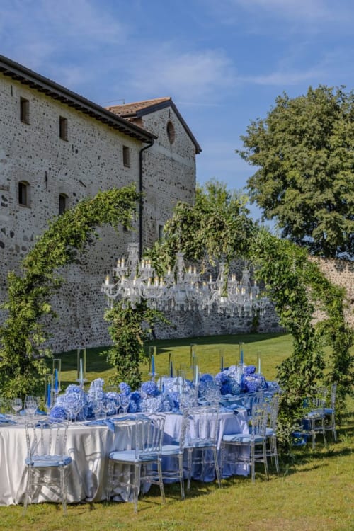 Elegante ricevimento di nozze all'aperto presso Corte Baruzzo Relais a Volta Mantovana con decorazioni floreali blu e castello in pietra