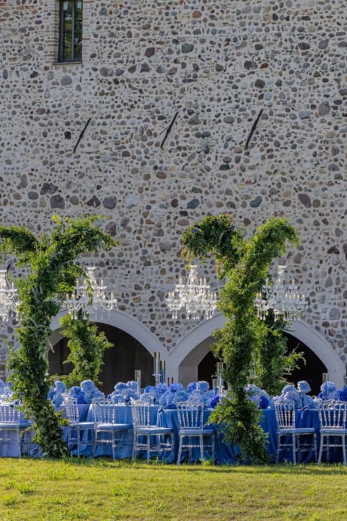 Elegante allestimento da pranzo all'aperto presso Corte Baruzzo Relais con ortensie blu, colonne rampicanti e sfondo in pietra