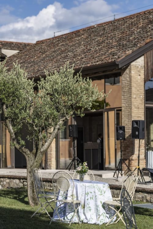 Spazio pranzo all'aperto presso Corte Baruzzo Relais con ulivo, edifici in pietra e cielo blu a Volta Mantovana