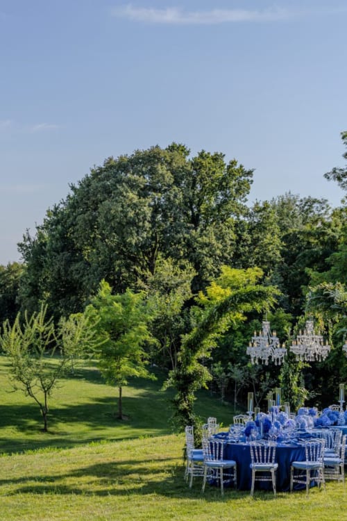 Elegante ricevimento di nozze all'aperto presso Corte Baruzzo Relais con tavoli rivestiti di blu sotto alberi maestosi a Volta Mantovana