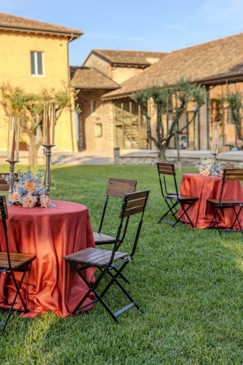 Elegante allestimento per cena all'aperto presso Corte Baruzzo Relais con tavoli drappeggiati in rosso, candelabri e vista sulla villa toscana a Volta