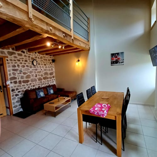 Spacieuse salle à manger du gîte avec poutres en bois, murs en pierre et sièges confortables aux Gîtes Du Couvent