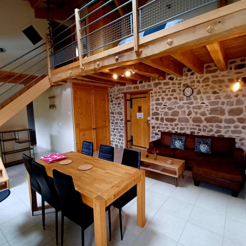 Séjour ouvert aux gîtes du Couvent avec table à manger, canapé et murs en pierre, Ardèche