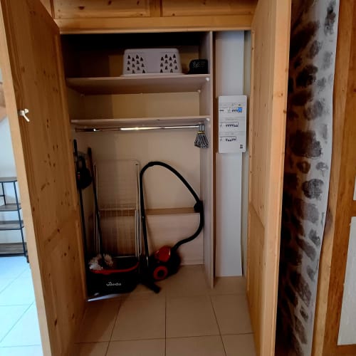 Placard en bois ouvert avec étagères, équipements de nettoyage, panneau électrique et articles de rangement aux Gîtes Du Couvent