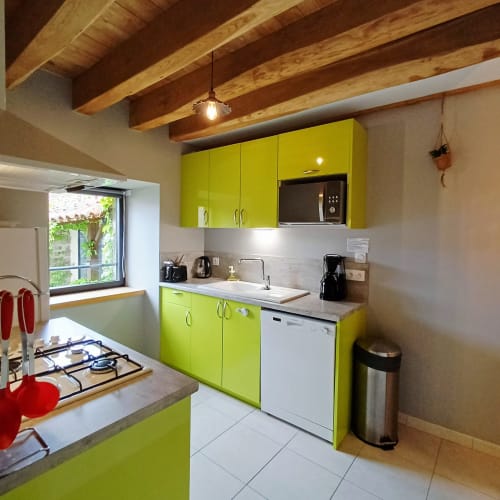 Cuisine moderne avec armoires vert citron éclatant, cuisinière à gaz et plafond aux poutres apparentes au gîte Les Gîtes Du Couvent