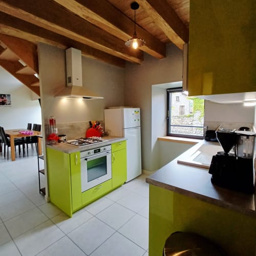 Cuisine moderne avec armoires vert citron, électroménagers en acier inoxydable et poutres en bois apparent au gîte Les Gîtes Du Couvent