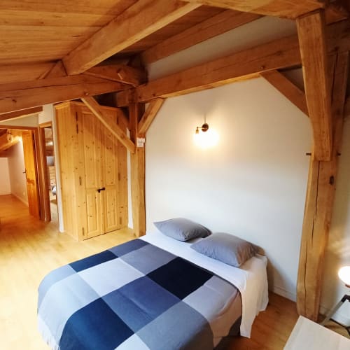 Chambre douillette du gîte 1 avec parure à carreaux bleus, poutres en bois, portes en pin et murs blancs aux Gîtes Du Couvent