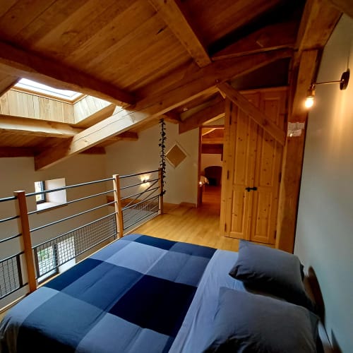 Chambre mansardée aux poutres en bois, mezzanine, literie bleue et garde-corps métallique aux Gîtes Du Couvent