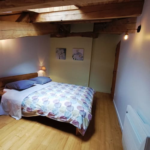 Chambre douillette sous les toits aux Gîtes Du Couvent avec poutres en bois, lit queen-size, coussins bleus et murs jaunes à Nozières, Ardèche