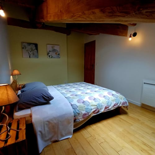 Chambre chaleureuse aux Gîtes Du Couvent avec literie à motifs, poutres en bois, murs jaunes et lampe de chevet
