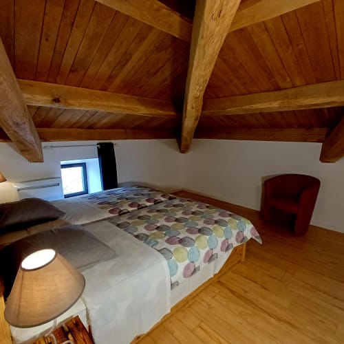 Chambre mansardée cosy aux poutres apparentes, lit queen-size avec literie colorée, fauteuil rouge et fenêtre de toit aux Gîtes