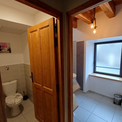 Salle de bain du gîte Les Gîtes Du Couvent en Ardèche avec porte en bois, toilettes et fenêtre