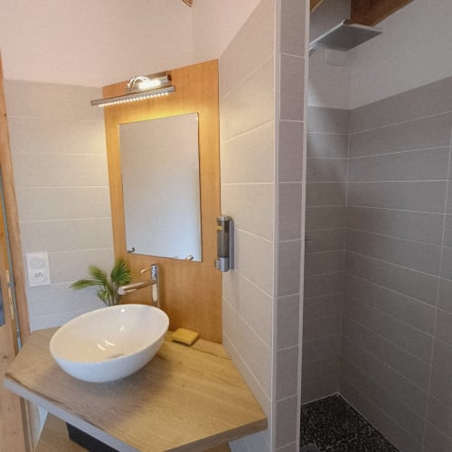 Salle de bain moderne du gîte 2 avec vasque blanche, meuble en bois, miroir éclairant et douche spacieuse
