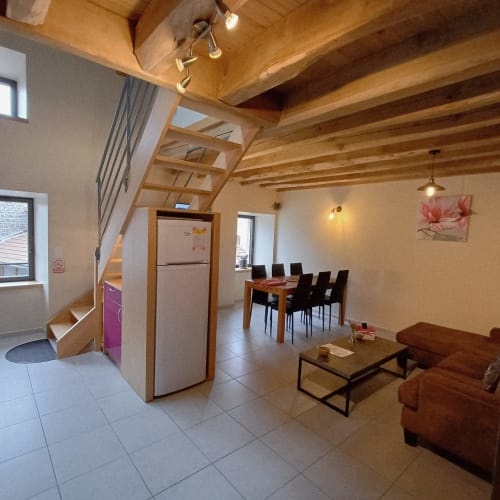 Spacieux séjour de cottage avec poutres en bois apparent, table à manger, canapé marron, cuisine avec réfrigérateur et boiseries