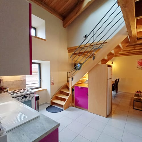 Intérieur cottage moderne ouvert avec escalier bois, touches violettes, cuisine équipée et salle à manger lumineuse aux