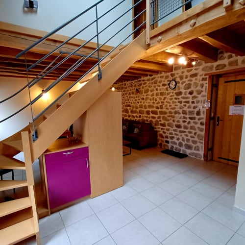 Intérieur de gîte moderne aux Gîtes Du Couvent avec escalier en bois, murs en pierre et meuble de cuisine violet