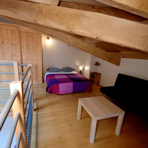 Chambre rustique aux Gîtes Du Couvent, Ardèche, avec poutres apparentes, literie colorée et équipements modernes.