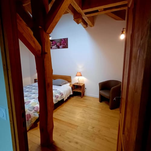 Chambre cosy du gîte Les Gîtes Du Couvent avec poutres en bois, lit à baldaquin et fauteuil marron en Ardèche