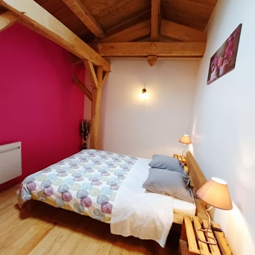 Chambre douillette aux Les Gîtes Du Couvent avec poutres apparentes, mur accent rose et vue sur les montagnes en Ardèche