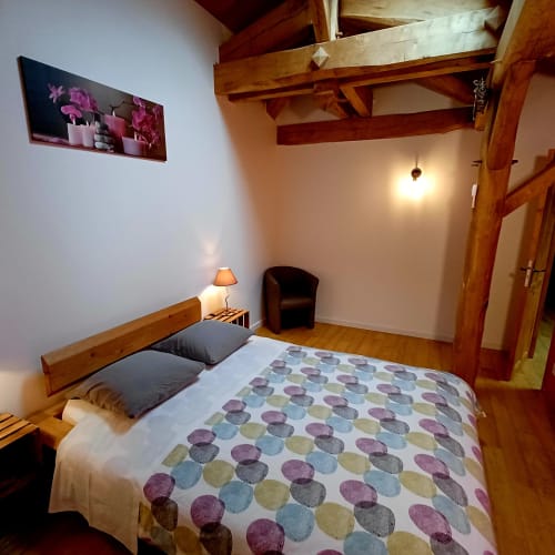 Chambre cosy du gîte Les Gîtes Du Couvent avec poutres en bois, lit queen-size et courtepointe à motifs
