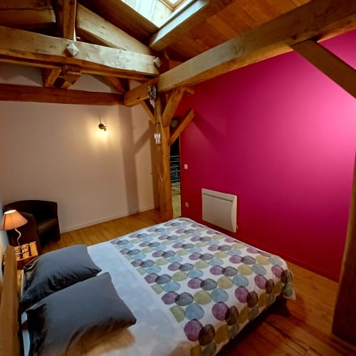 Chambre de style rustique avec poutres apparentes, mur d'accent rose, literie patterned et puit de lumière