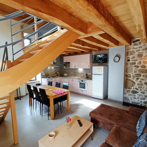 Cuisine et salle à manger de chaumière moderne avec poutres en bois apparentes, murs en pierre, table à manger en bois, mobilier rose et